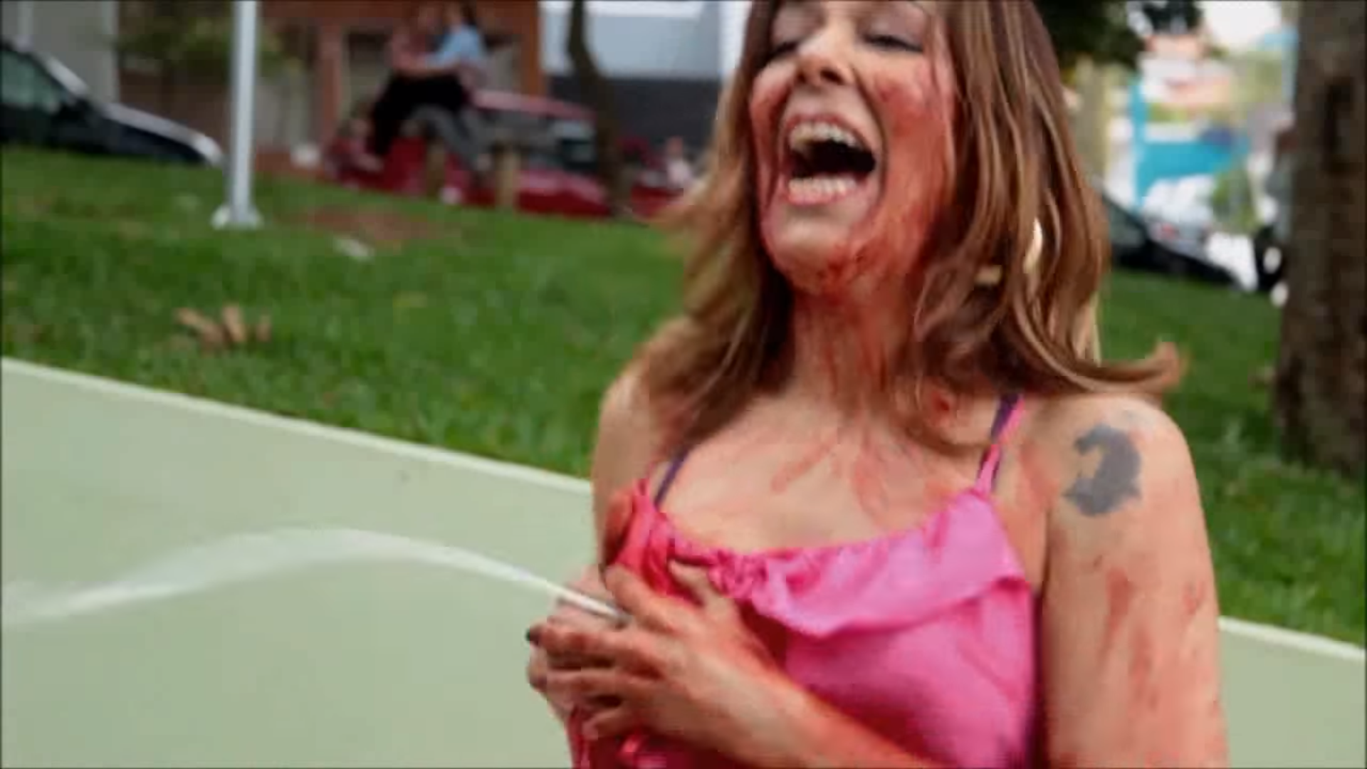 Uma mulher numa praça com o rosto e os braços ensanguentados, jorrando leite de um seio, através da roupa.