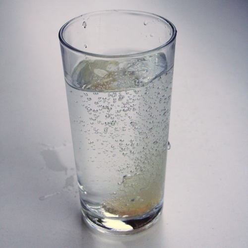 Copo com um comprimido efervescente soltando bolhas dentro da água