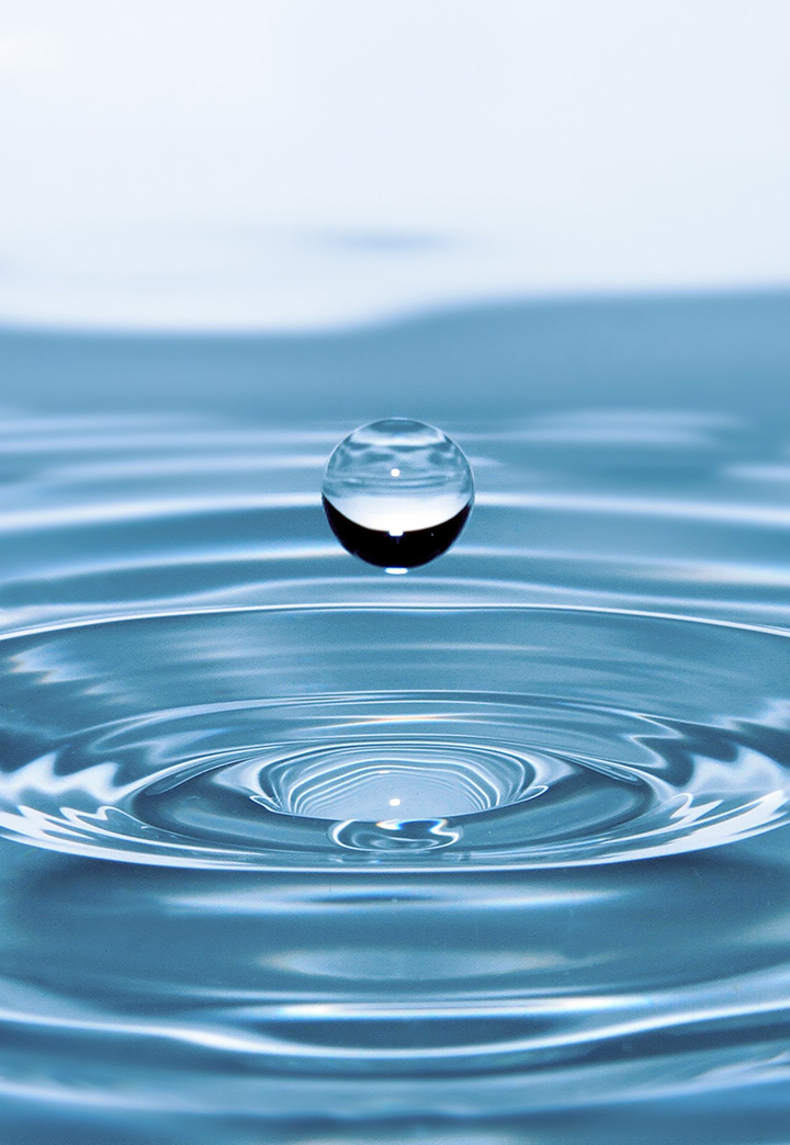 Uma gota esférica de água acima de uma superfície de água com ondas circulares.